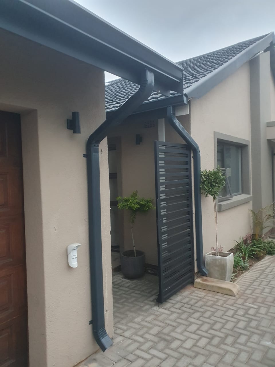 Finished charcoal gutter and downpipe installation at a residential entrance